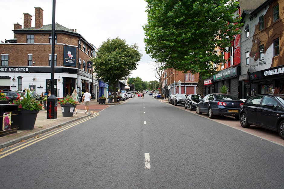 An aerial view of a street in Hornchurch showing a row of small commercial buildings with shops and offices, including a plant and gift shop with outdoor displays. Several cars, including a white van 